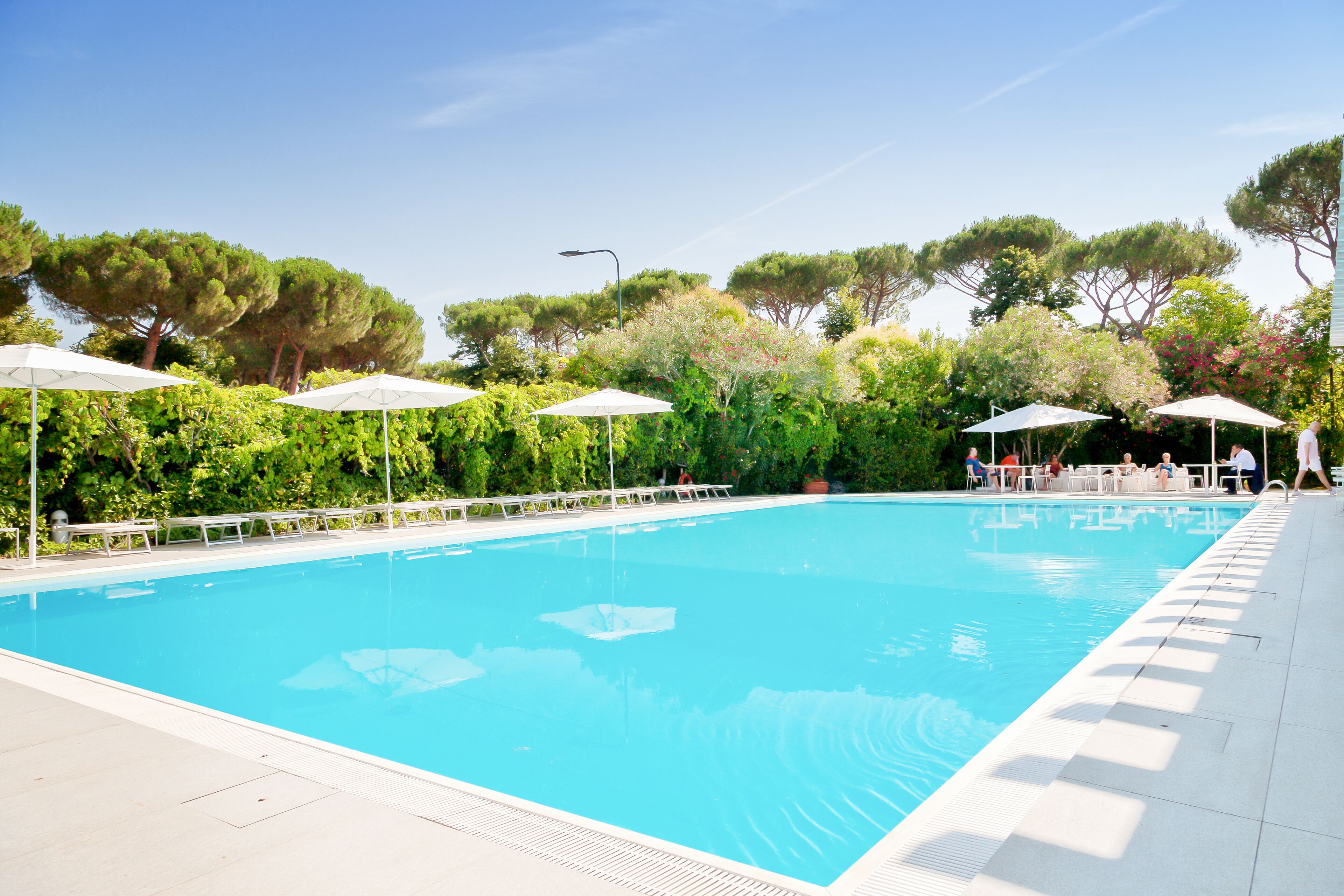 Una piscina con sombrillas blancas y sillas de descanso, rodeada de follaje y árboles.