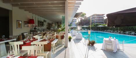 A poolside restaurant with outdoor seating, a pool, and a view of the cityscape.