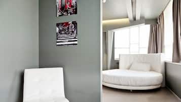 A modern bedroom with a white chair, a round bed, and two framed artworks on the wall.