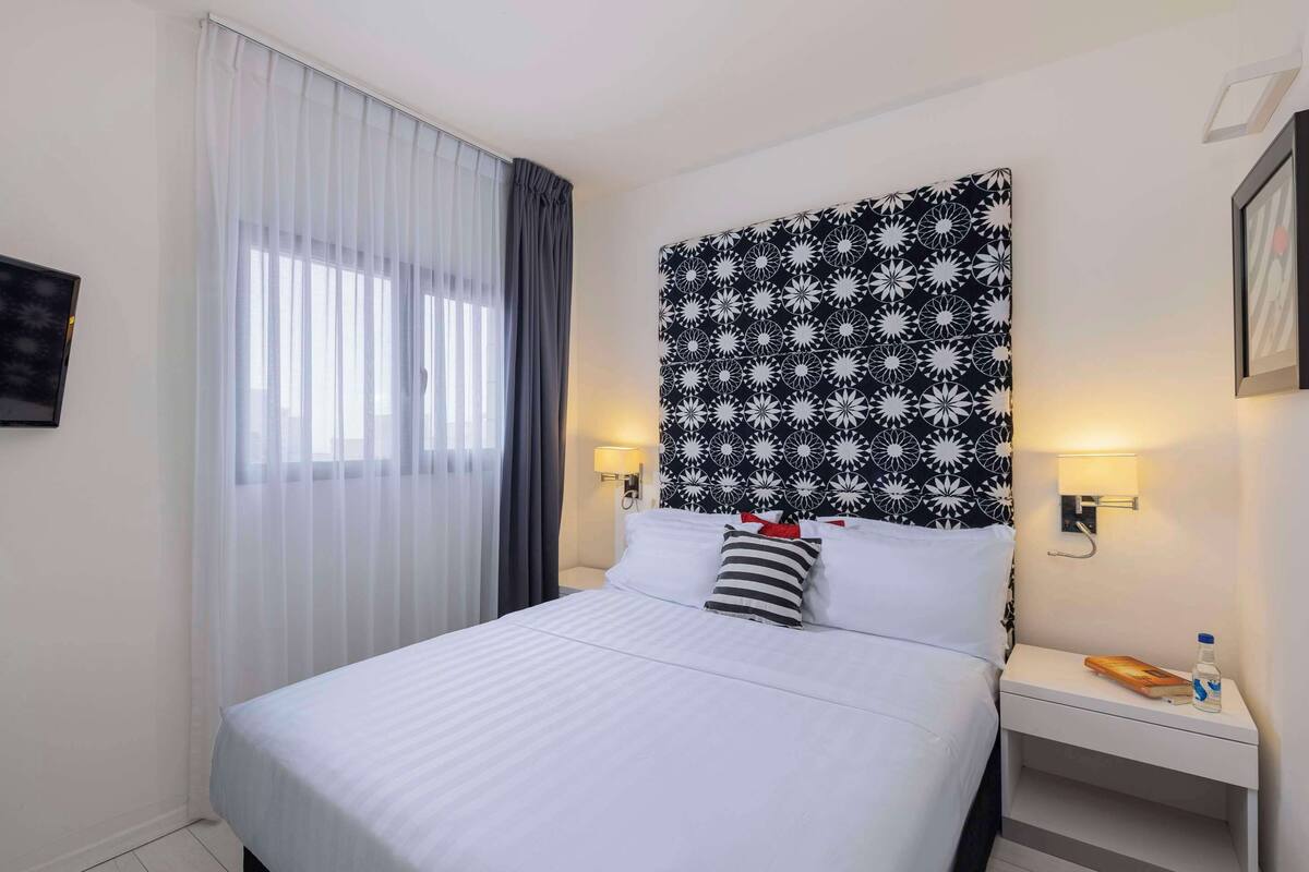 A hotel room with a bed, a nightstand, a lamp, and a wall-mounted TV.