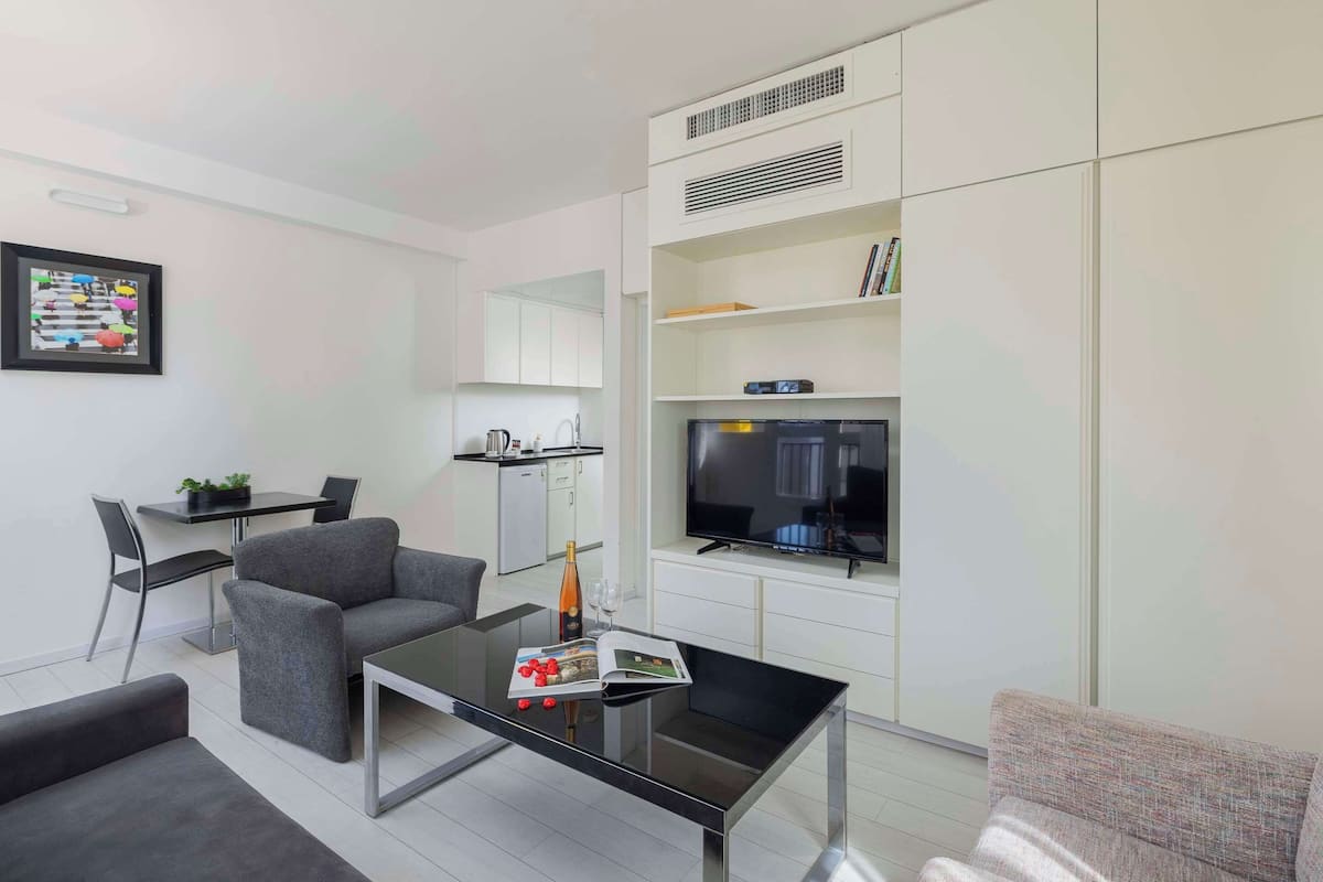 A modern living room with a sofa, a coffee table, a TV, and a kitchen area.