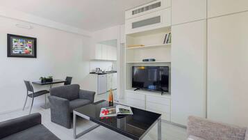 A modern living room with a sofa, a coffee table, a TV, and a kitchen area.