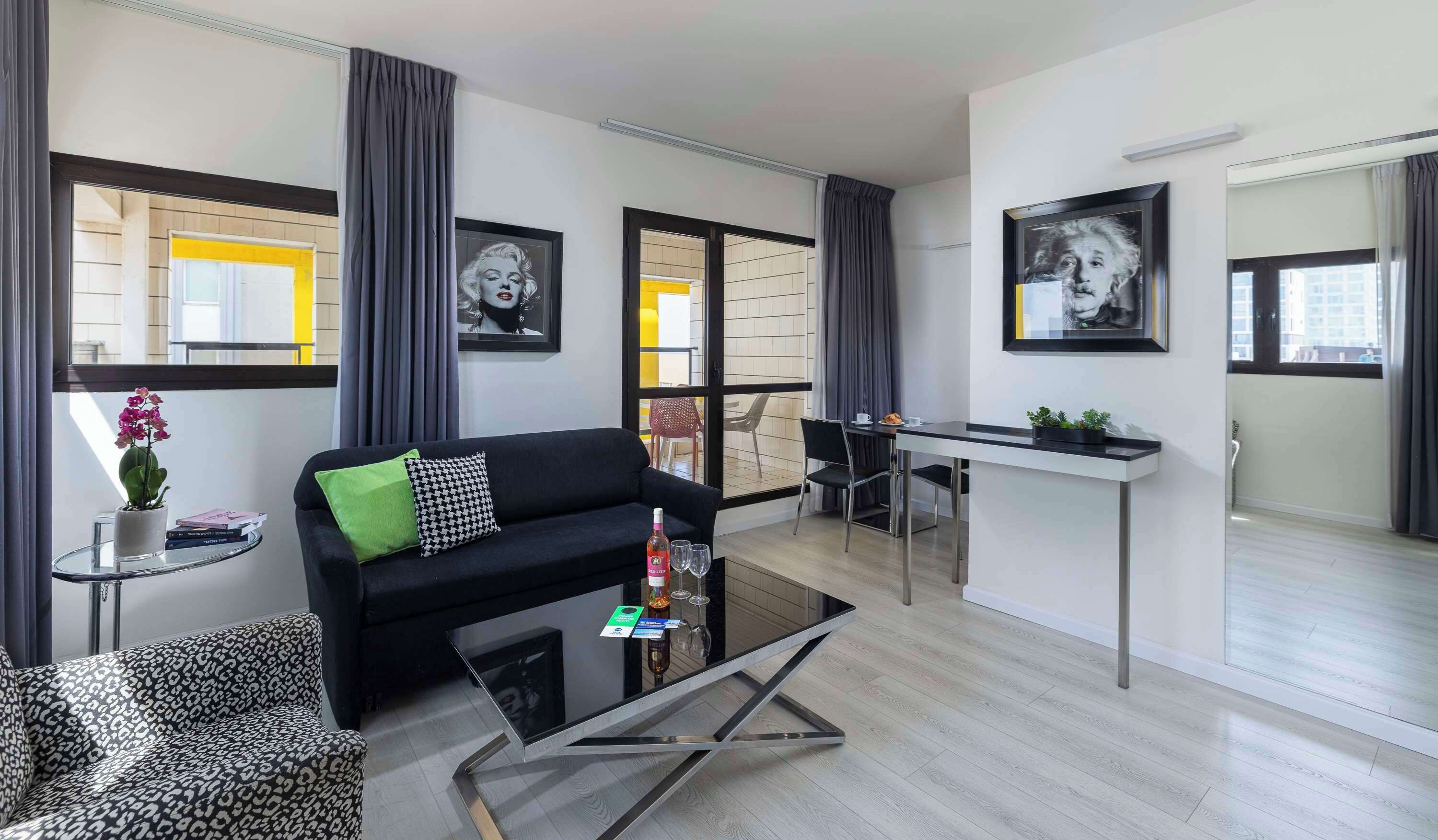 A modern living room with a black sofa, a glass coffee table, and a dining area with a white table and chairs.