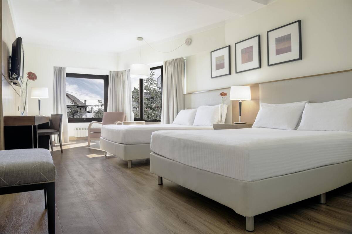 Habitación de hotel con dos camas, un escritorio, una silla y una ventana con cortinas.