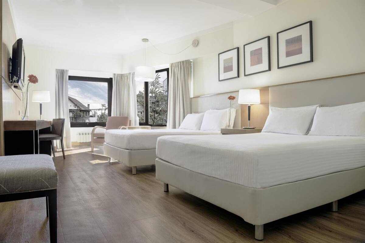 Habitación de hotel con dos camas, un escritorio, una silla y vistas al exterior.