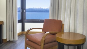 Una habitación con vistas a un lago y montañas, una silla de madera y una pequeña mesa redonda.