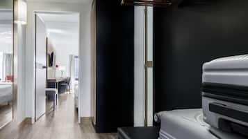A modern hotel room with a bed, a desk, and a chair. There is a large window and a door leading to another room.