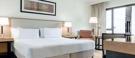 Una habitación de hotel con una cama grande, dos mesitas de noche, un escritorio, una silla y una ventana con cortinas.