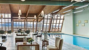 Un espacio interior amplio con piscina, techo de madera y grandes ventanales con vistas a las montañas.