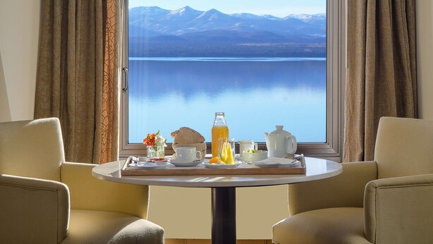 Una mesa de comedor con alimentos para el desayuno y vistas a un lago con montañas al fondo.