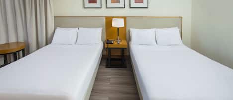 A hotel room with two single beds, a wooden nightstand with a lamp, a telephone, and a small table.