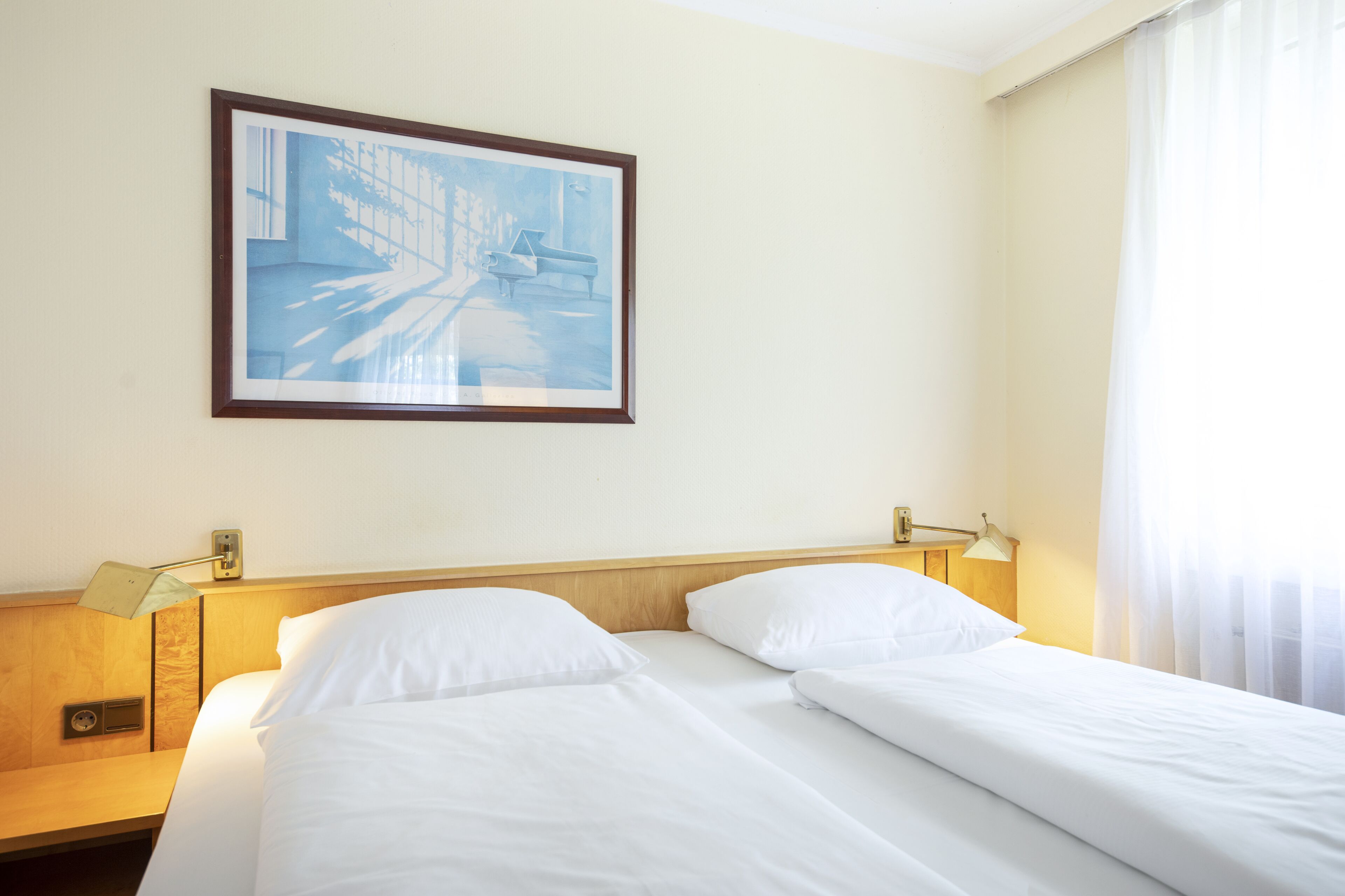 A hotel room with two beds, a painting on the wall, and a window with curtains.