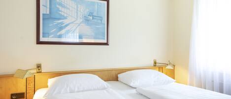 A hotel room with two beds, a painting on the wall, and a window with curtains.