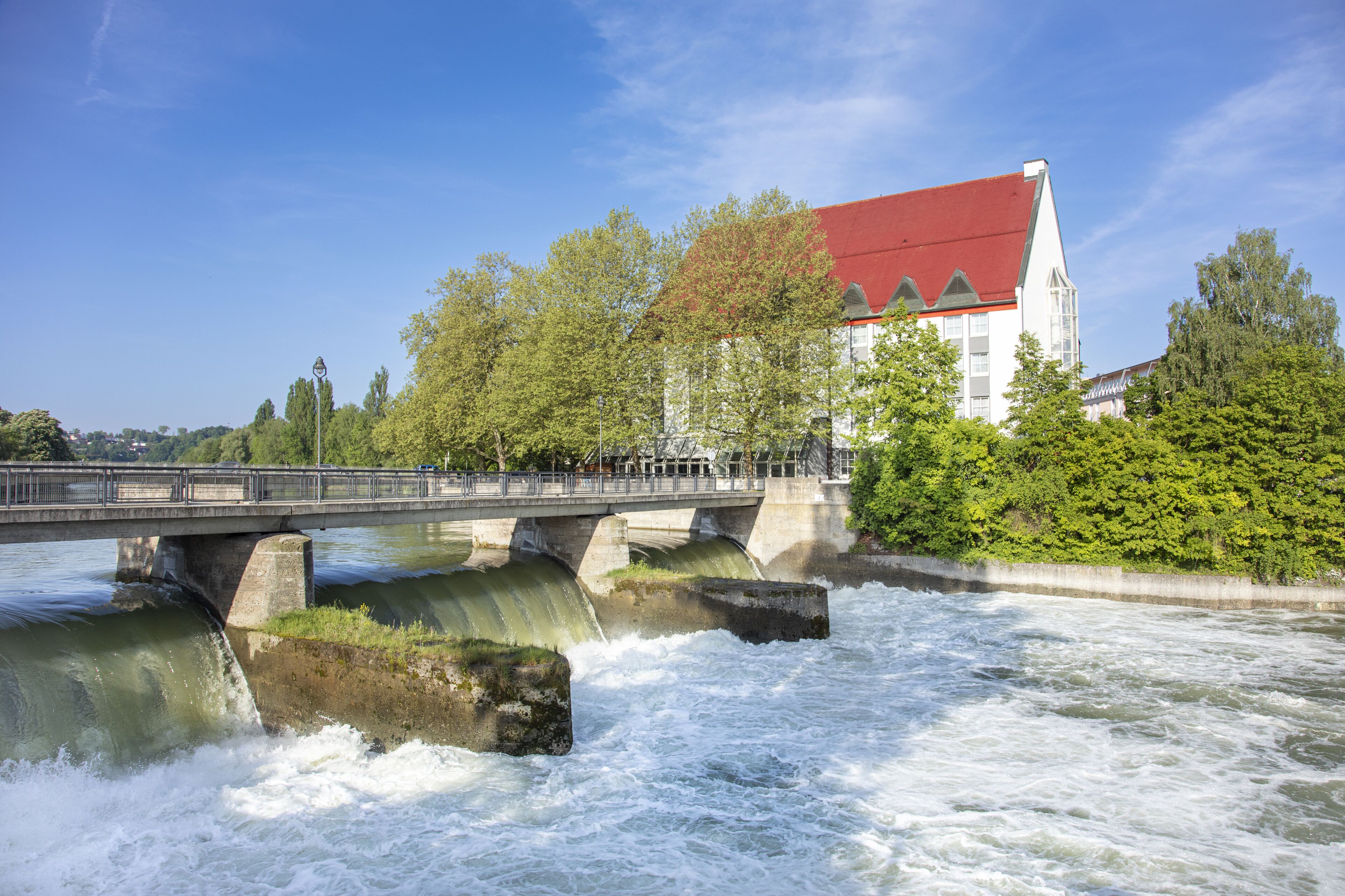 Un ponte sopra un fiume, con un edificio dal tetto rosso sullo sfondo.