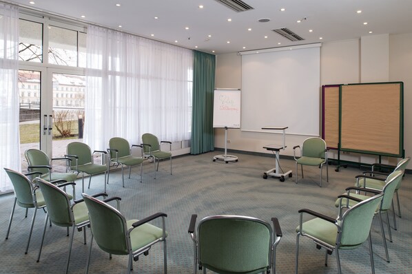 A conference room with green chairs arranged in a semi-circle, a whiteboard, and a projector screen.