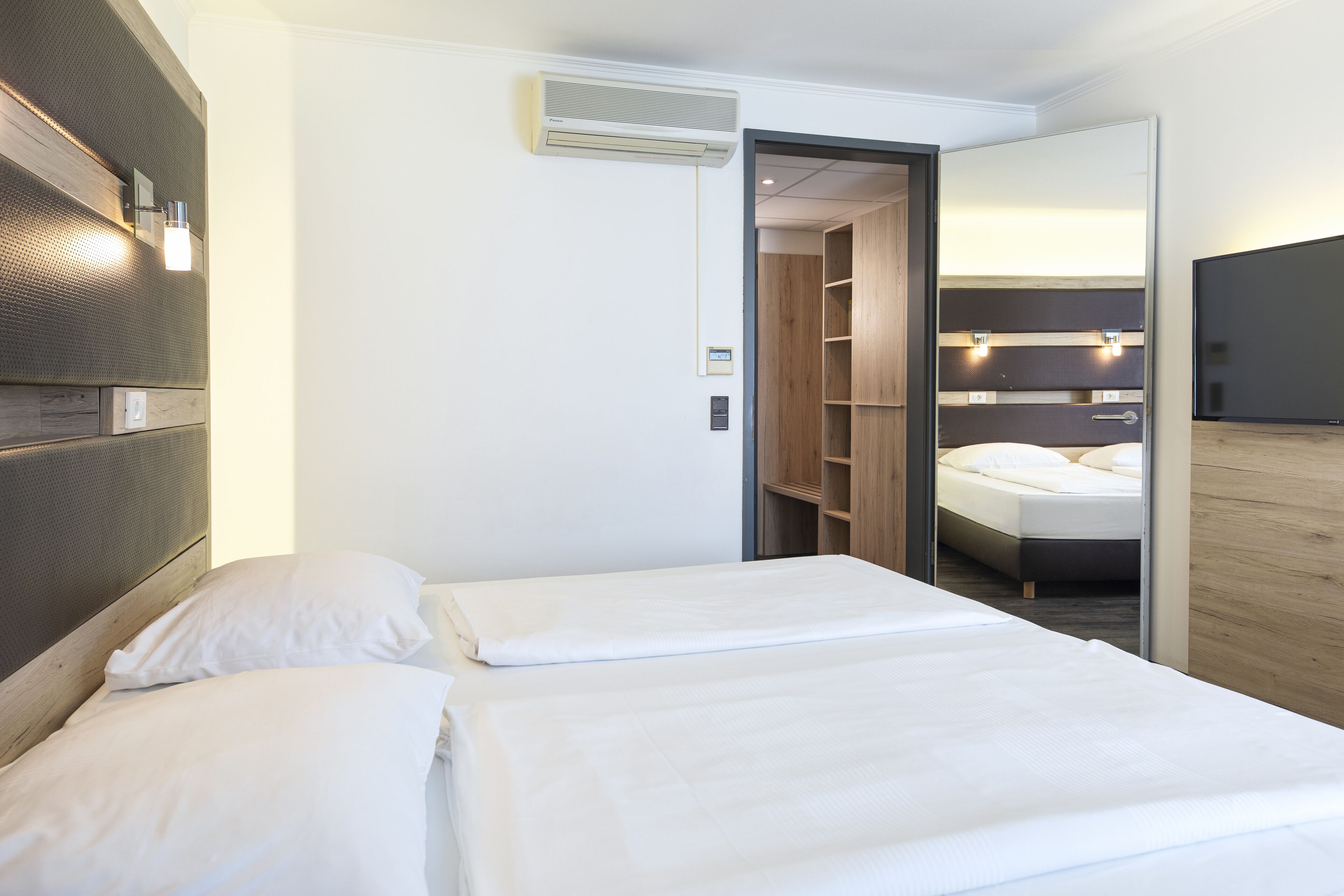 Une chambre d’hôtel avec deux lits, une armoire, un miroir et un téléviseur.