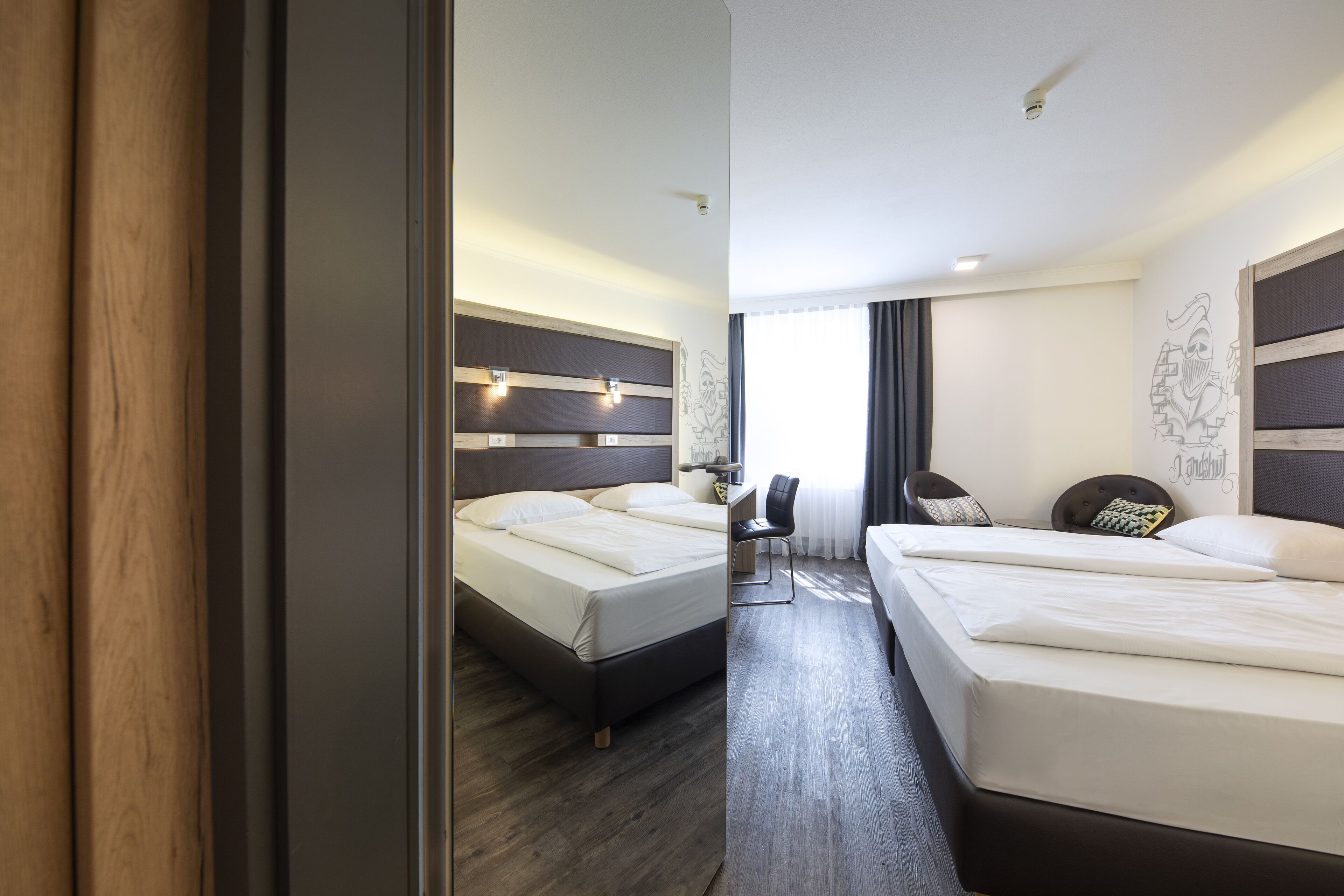 A hotel room with two beds, a desk, and a chair.