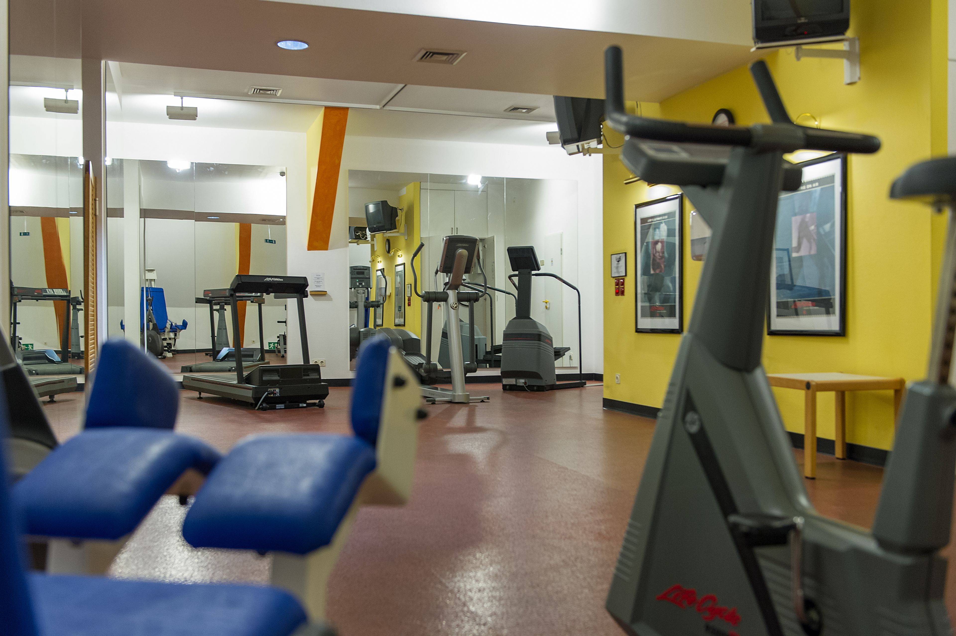 Ein Fitnessraum mit Trainingsgeräten, Spiegeln und einer gelben Wand.