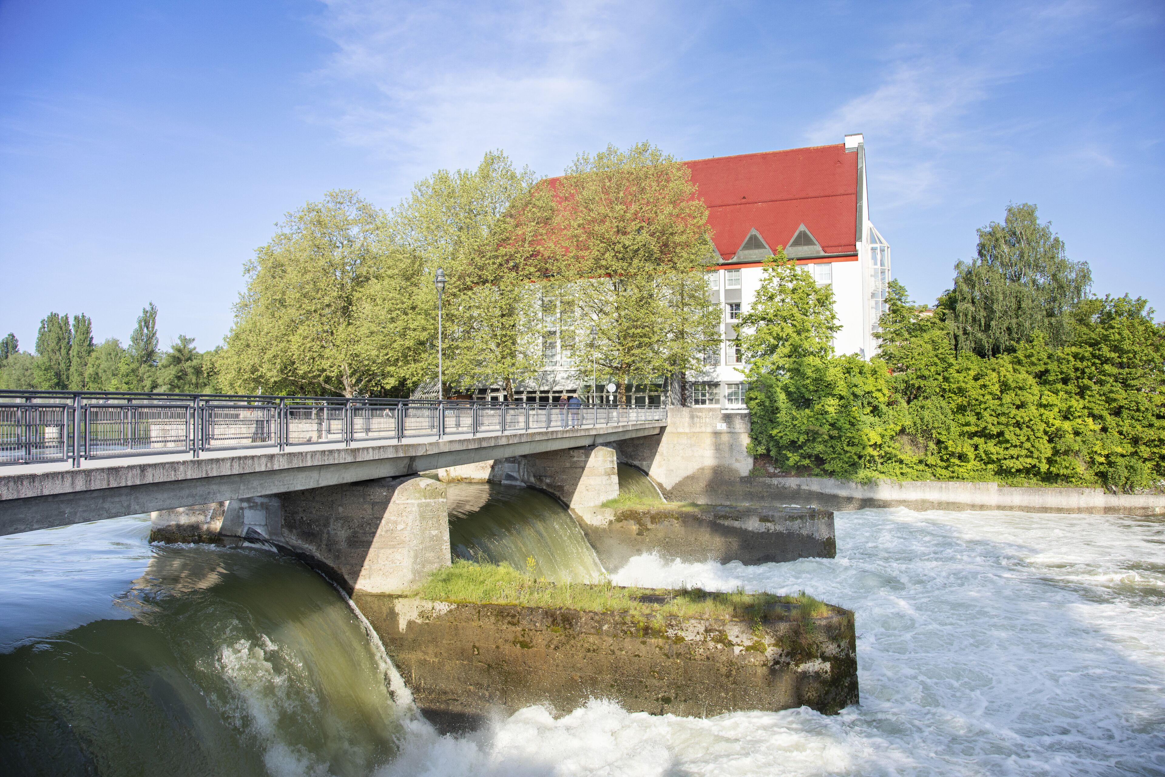 A bridge over a river with a building with a red roof in the background.