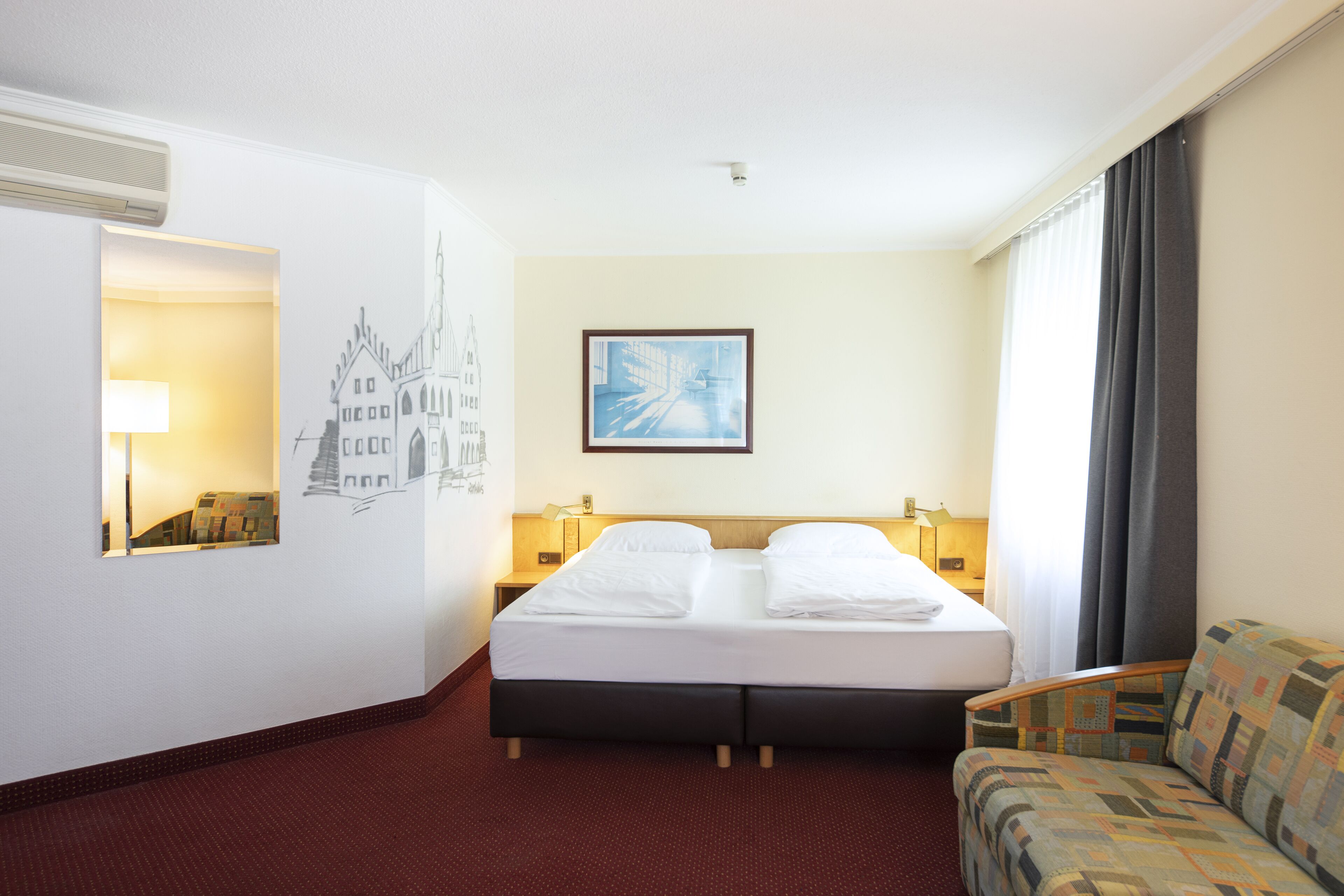Una habitación de hotel con una cama, una silla, un cuadro y una lámpara.