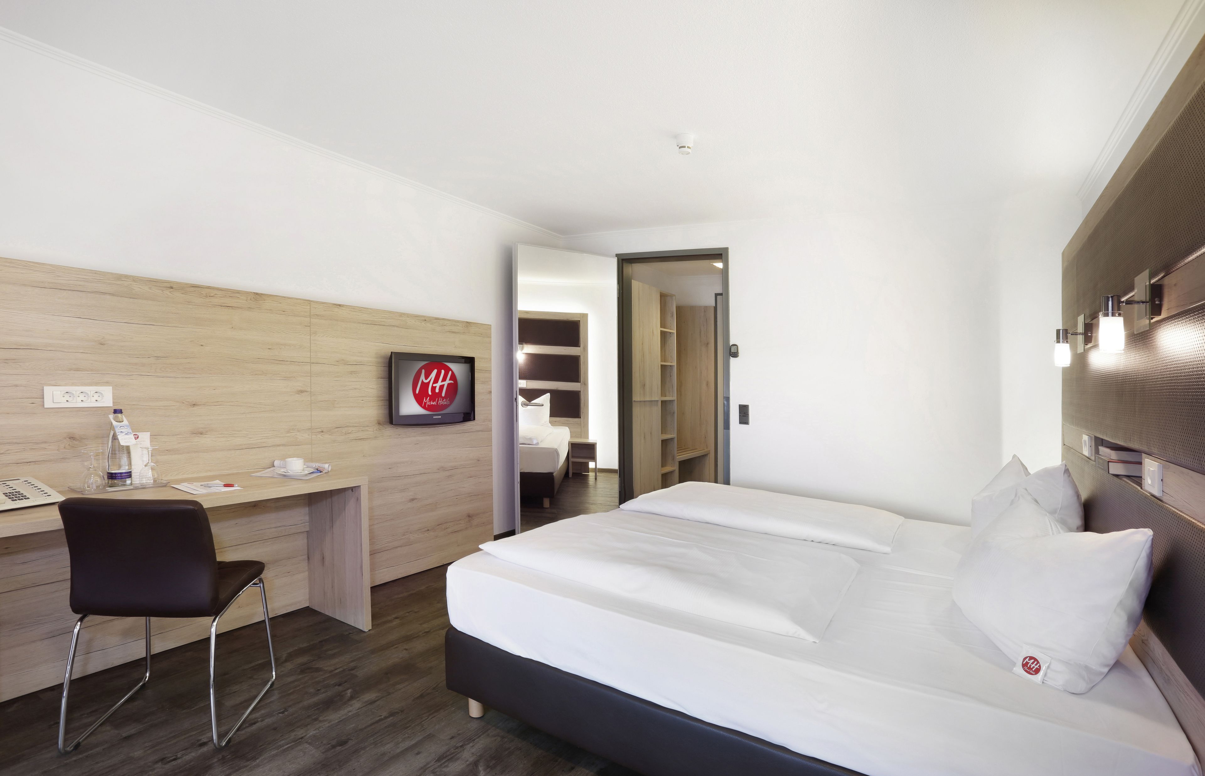 Une chambre d’hôtel avec un lit, un bureau, une chaise et une armoire.