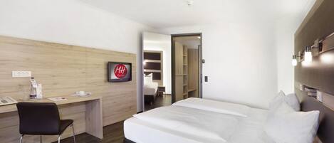 Une chambre d’hôtel avec un lit, un bureau, une chaise et une armoire.