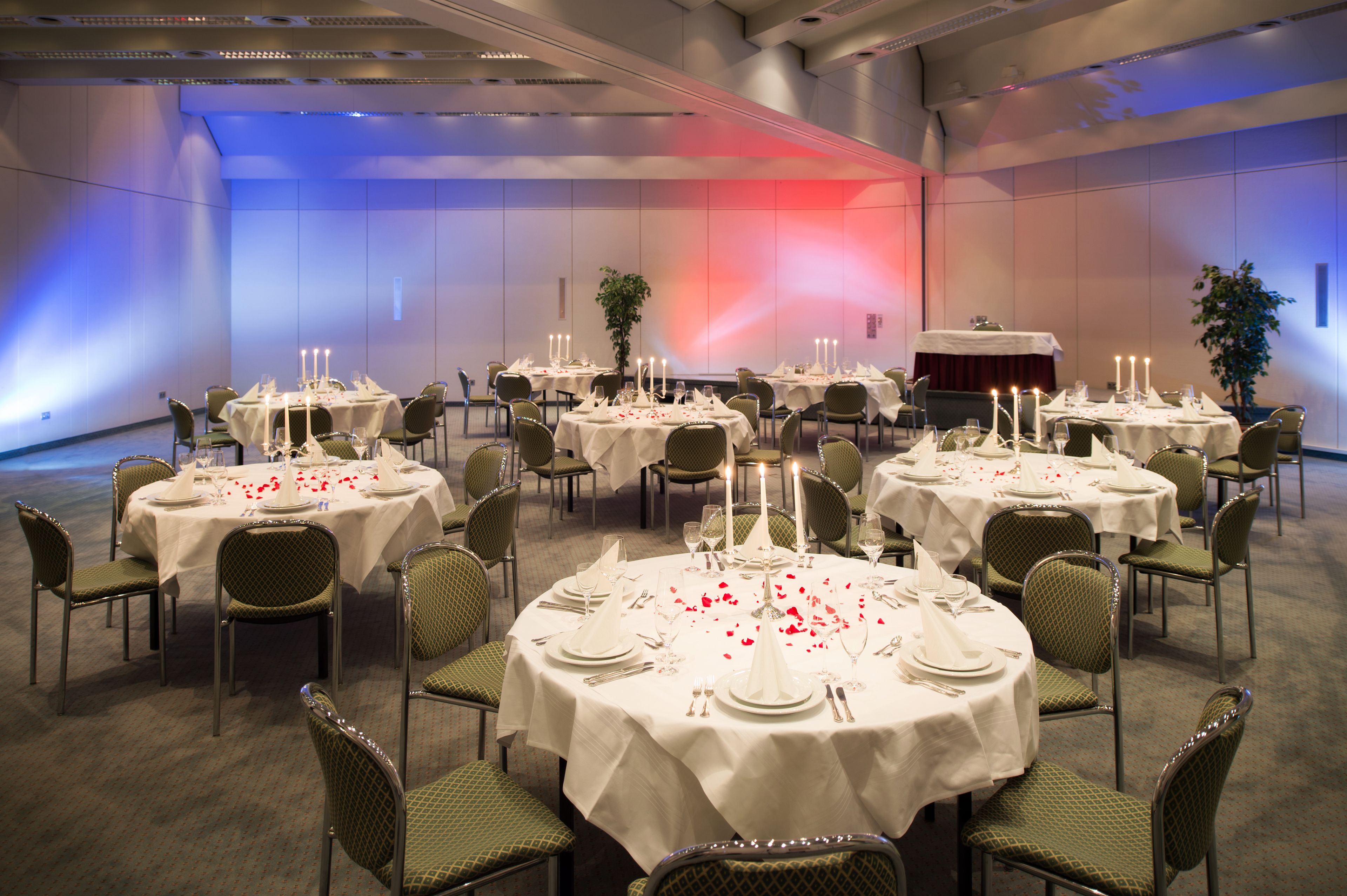 Un salón de banquetes con varias mesas redondas dispuestas para comer, cada una con mantel blanco y velas.
