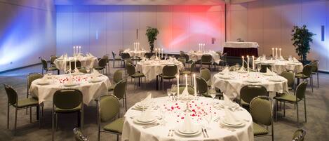 Un salón de banquetes con varias mesas redondas dispuestas para comer, cada una con mantel blanco y velas.