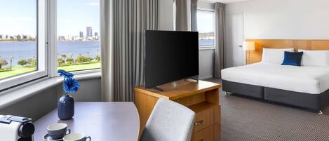 Hotelkamer met een bed, een bureau met een koffiezetapparaat en bekers, een televisie en uitzicht op een waterpartij.
