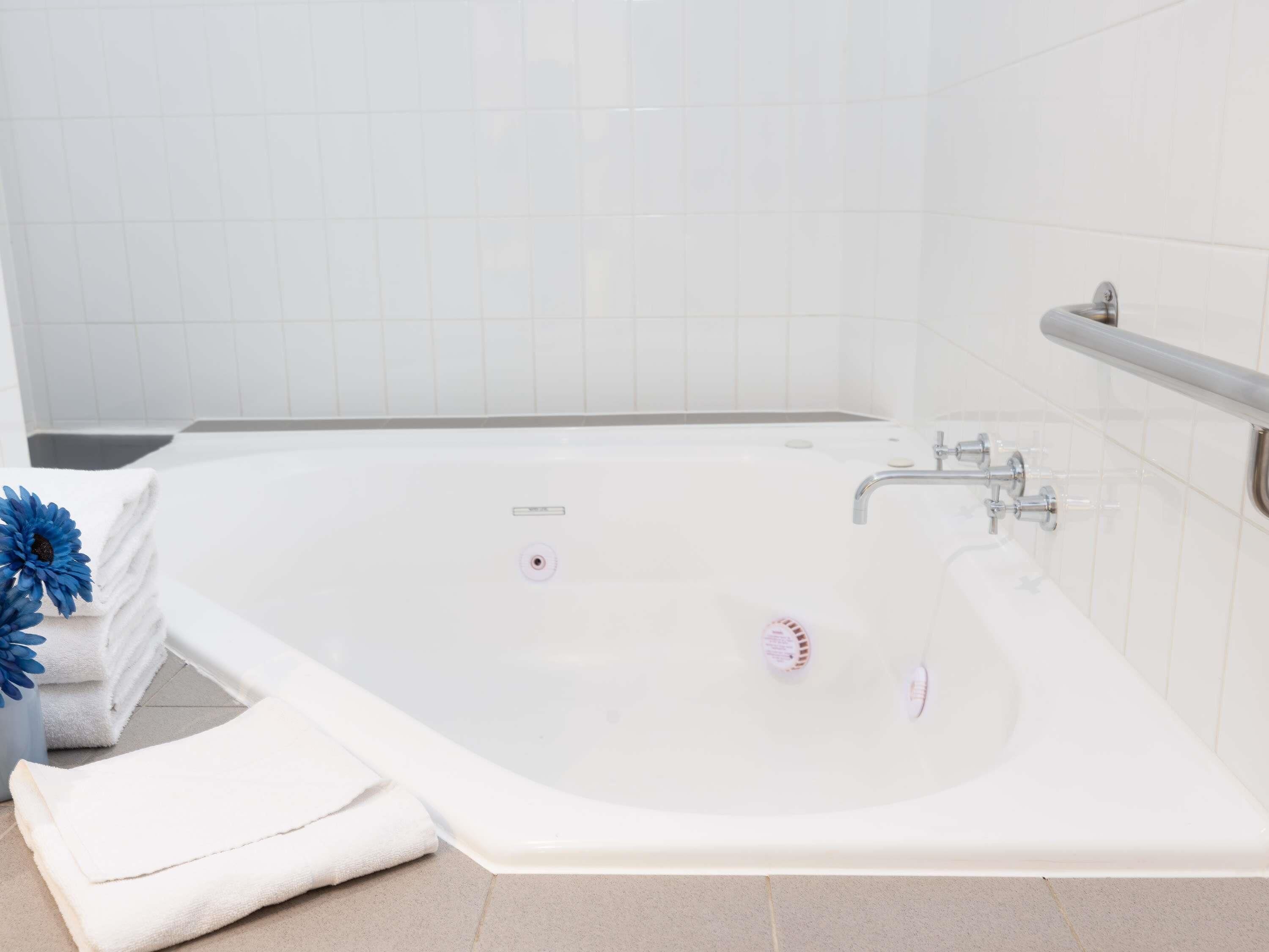 Un baño moderno con una bañera blanca, un pasamanos y una pila de toallas blancas.