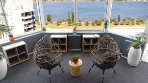 A room with two wicker chairs, a small wooden table, and a view of the sea and cityscape. - Novotel Perth Langley (Perth)