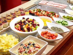 A buffet with various dishes including fruit salads, a pasta dish, and a bowl of sliced tomatoes.