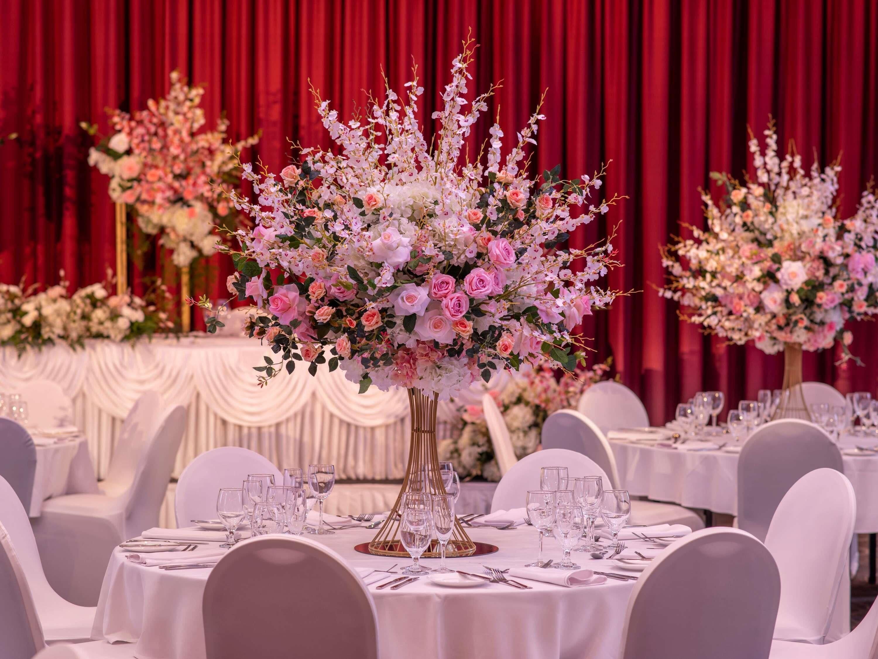A banquet hall with round tables set for a formal event, featuring floral centerpieces and white tablecloths.