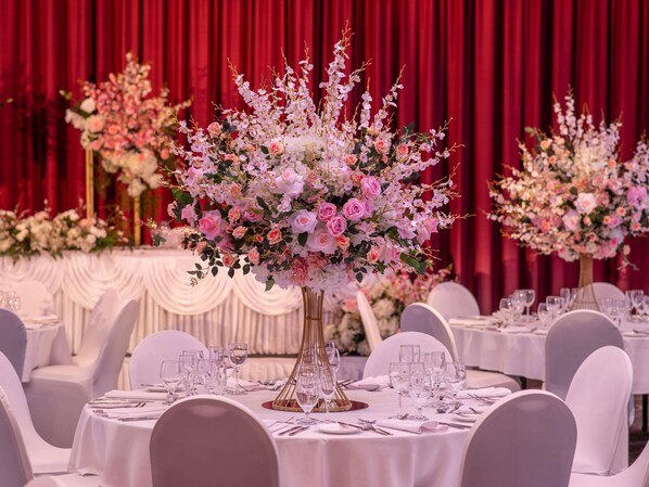 A banquet hall with round tables set for a formal event, featuring floral centerpieces and white tablecloths. - Novotel Perth Langley (Perth)
