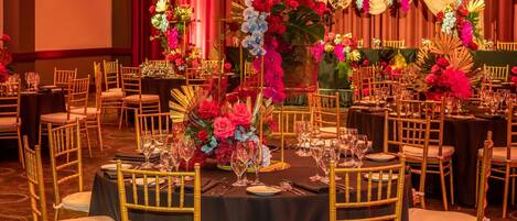 A banquet hall with round tables, gold chairs, and floral centerpieces.