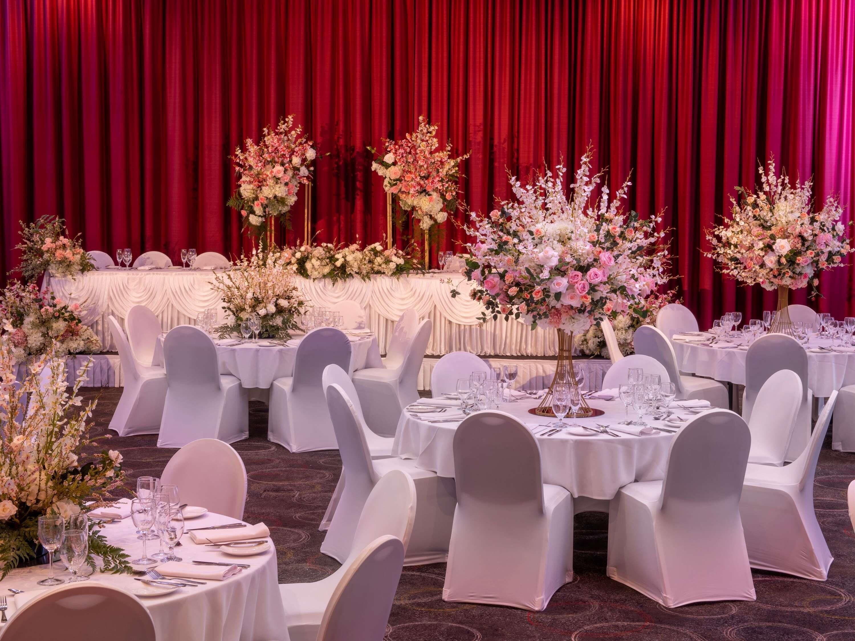 A banquet hall with round tables, white chairs, and red curtains.