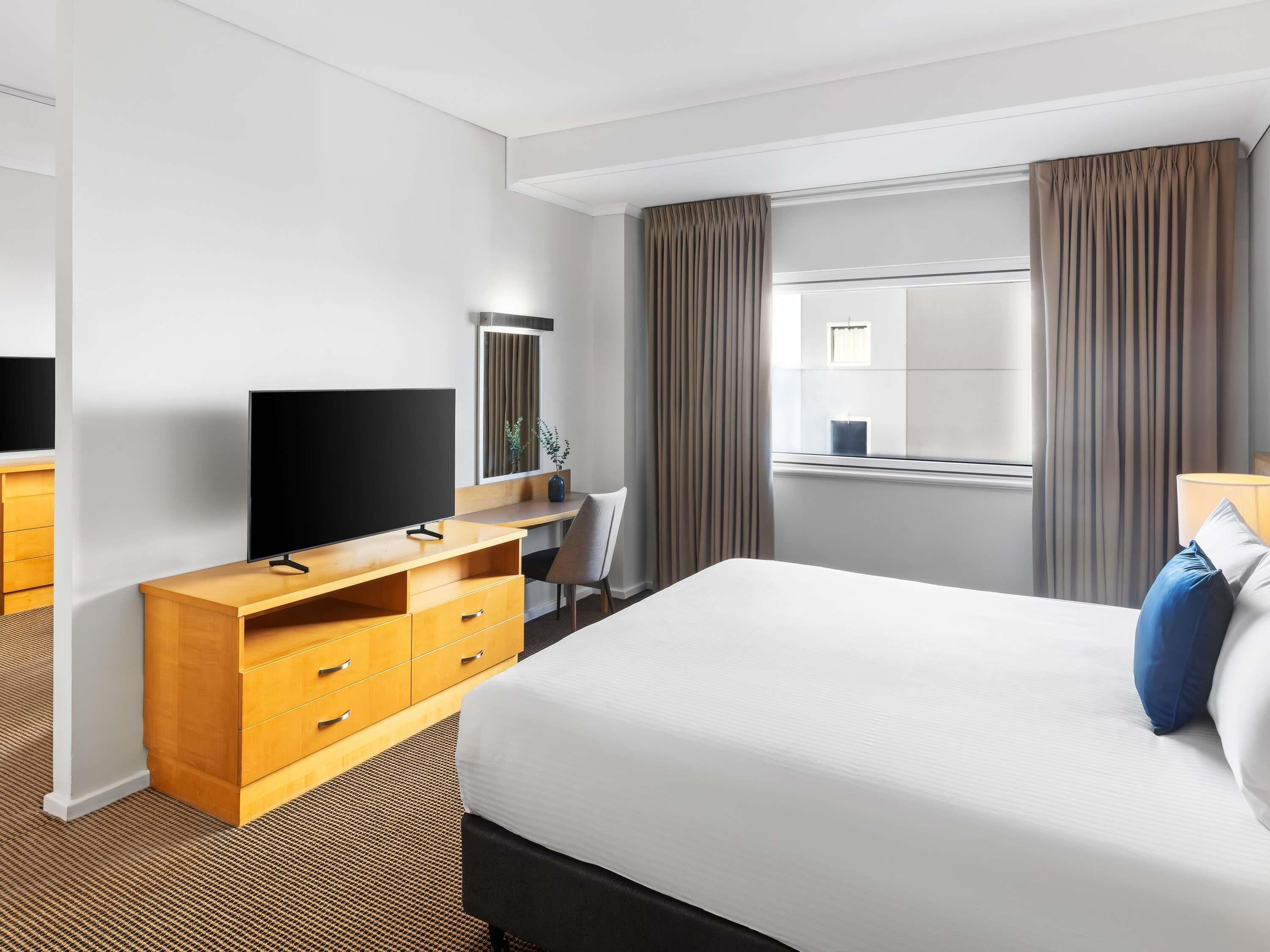 A hotel room with a bed, a TV, a desk, a chair, a window with curtains, and a mirror.