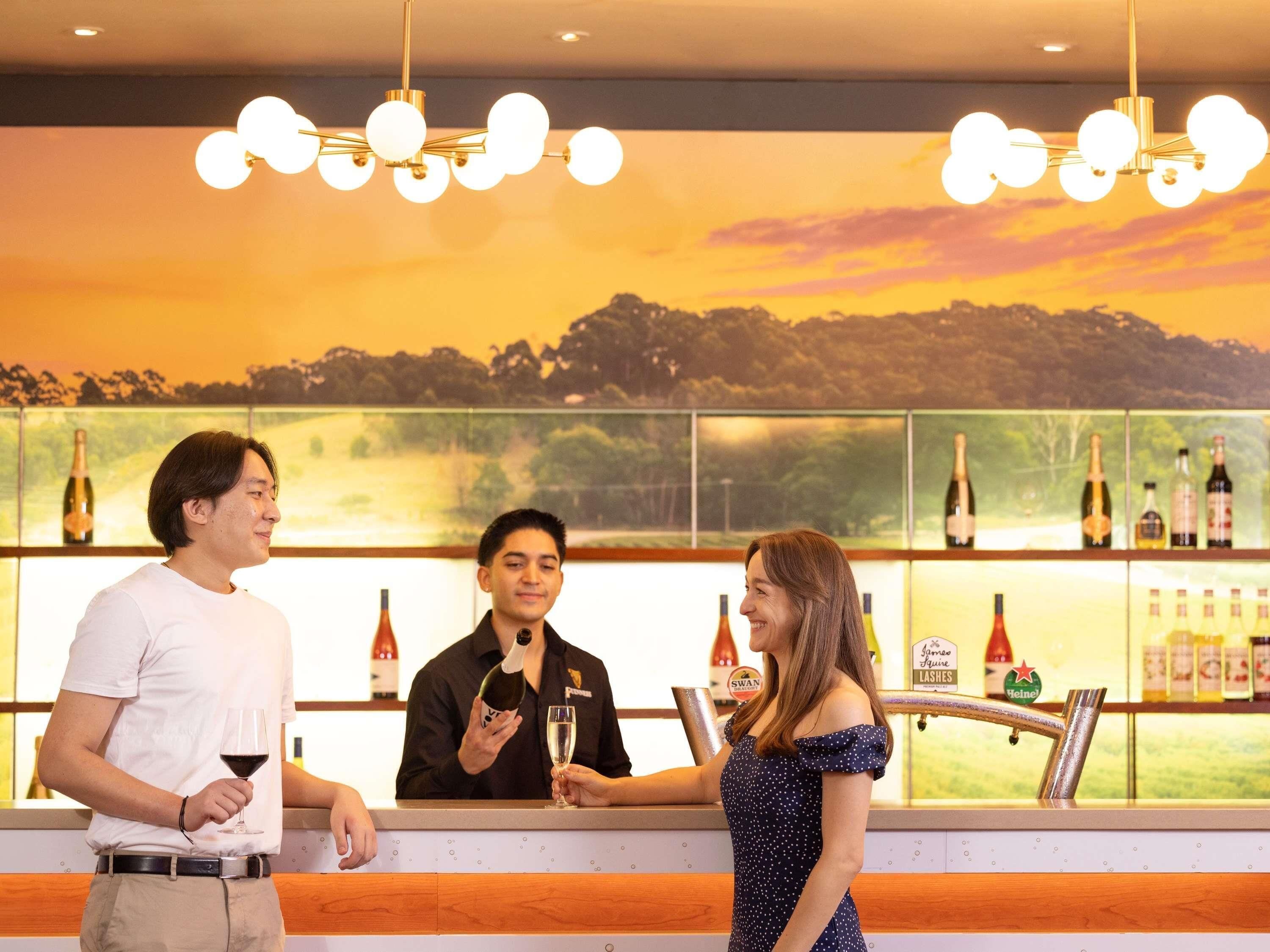 A bar area with a bartender and customers. There are bottles of alcohol on the shelves behind the bar.