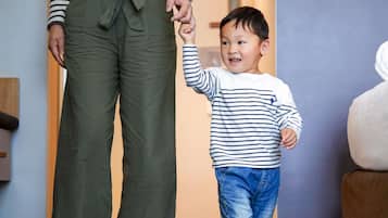 A person holding a child's hand in a room with a wooden floor and a brown couch.