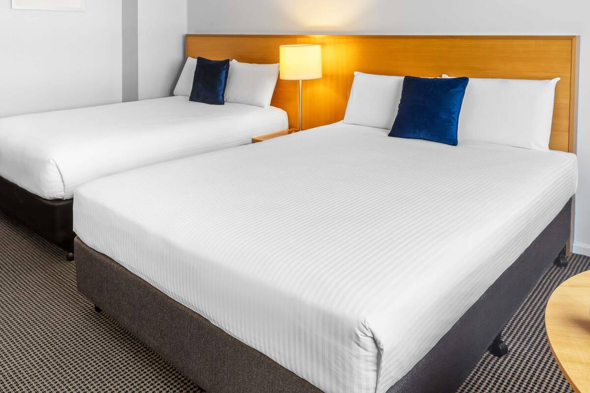 A hotel room with two beds, a wooden headboard, a nightstand with a lamp, and a framed picture on the wall.