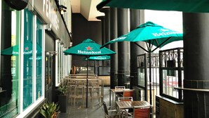 An outdoor seating area with tables and chairs, green umbrellas, and a building with large windows. - Novotel Perth Langley (Perth)