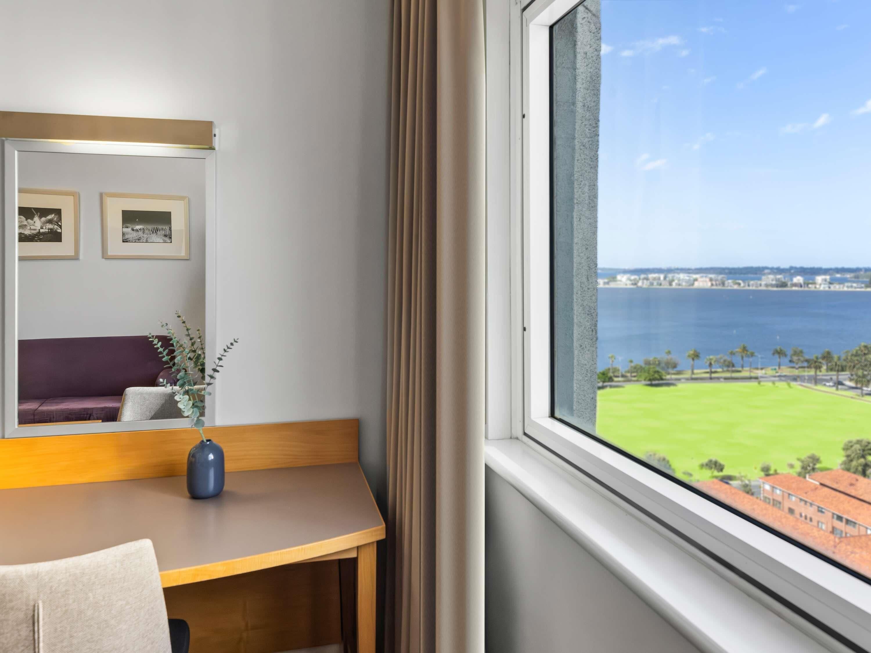 A hotel room with a view of the sea, a sofa, a desk, and framed pictures on the wall.