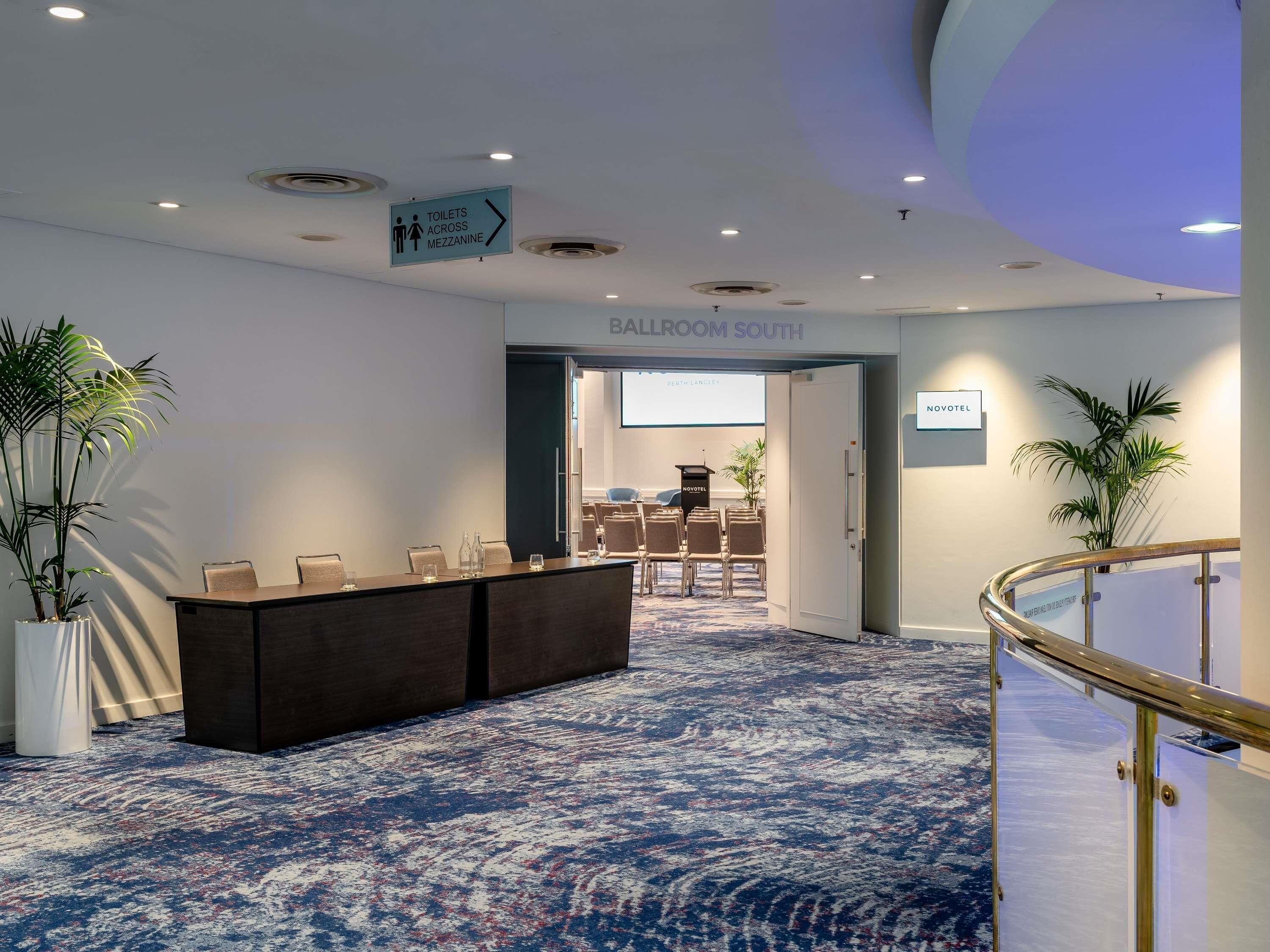 A hotel lobby with a reception desk, a sign for the ballroom, and a 'NOVOTEL' sign.