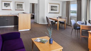 A hotel room with a dining area, a kitchenette, a seating area with a purple sofa, a coffee table, and a view of the outdoors.