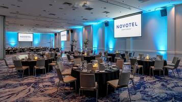A conference room at Novotel Perth Langley with multiple tables set for meetings, a large screen for presentations, and a carpeted floor.