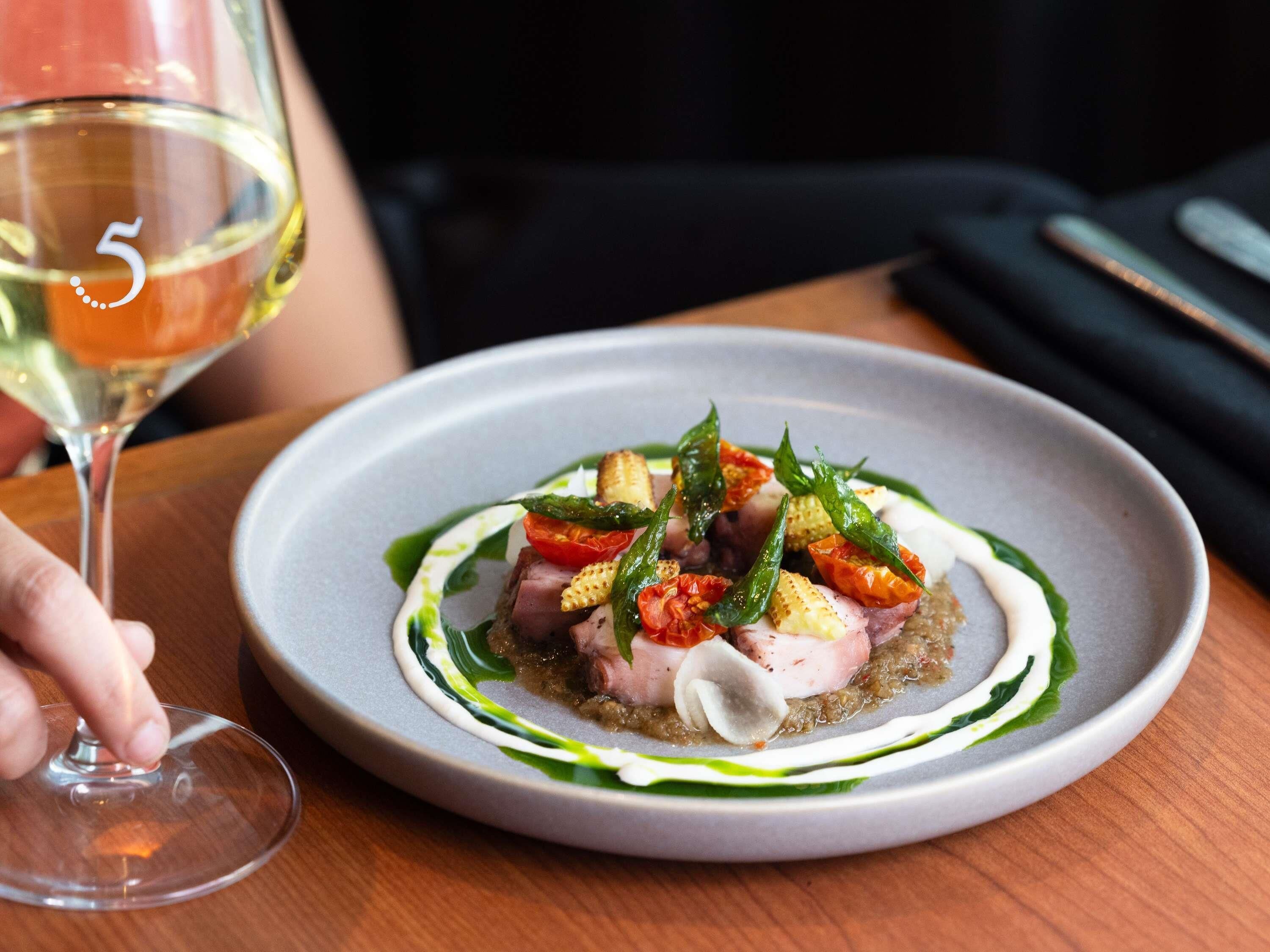 A plate of food with a glass of white wine on a wooden table.
