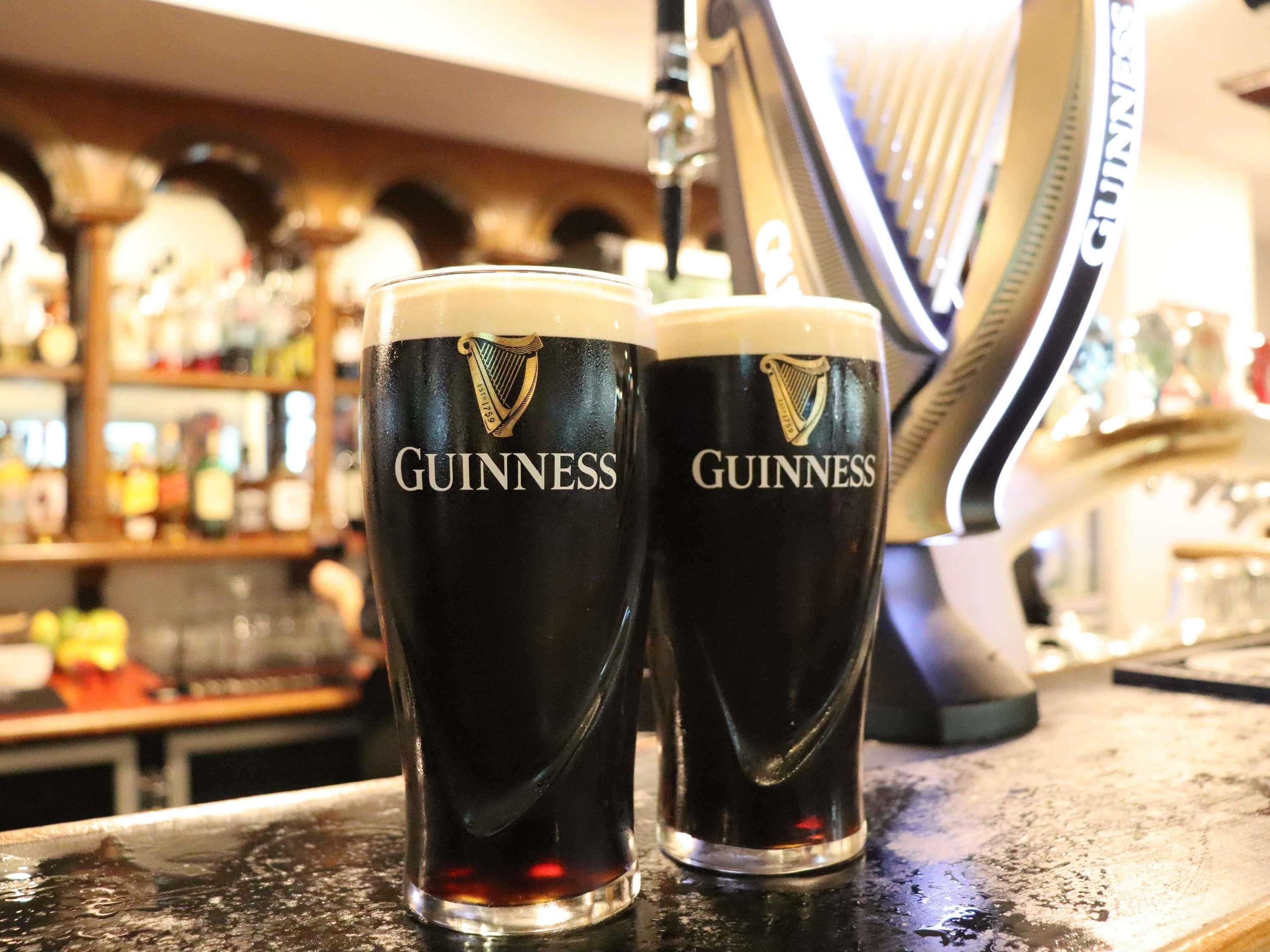 Zwei Guinness-Gläser auf einer Bar, im Hintergrund verschwommene Regale und Gegenstände.