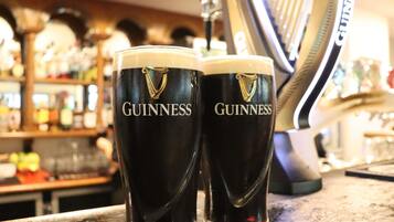 Zwei Guinness-Gläser auf einer Bar, im Hintergrund verschwommene Regale und Gegenstände.