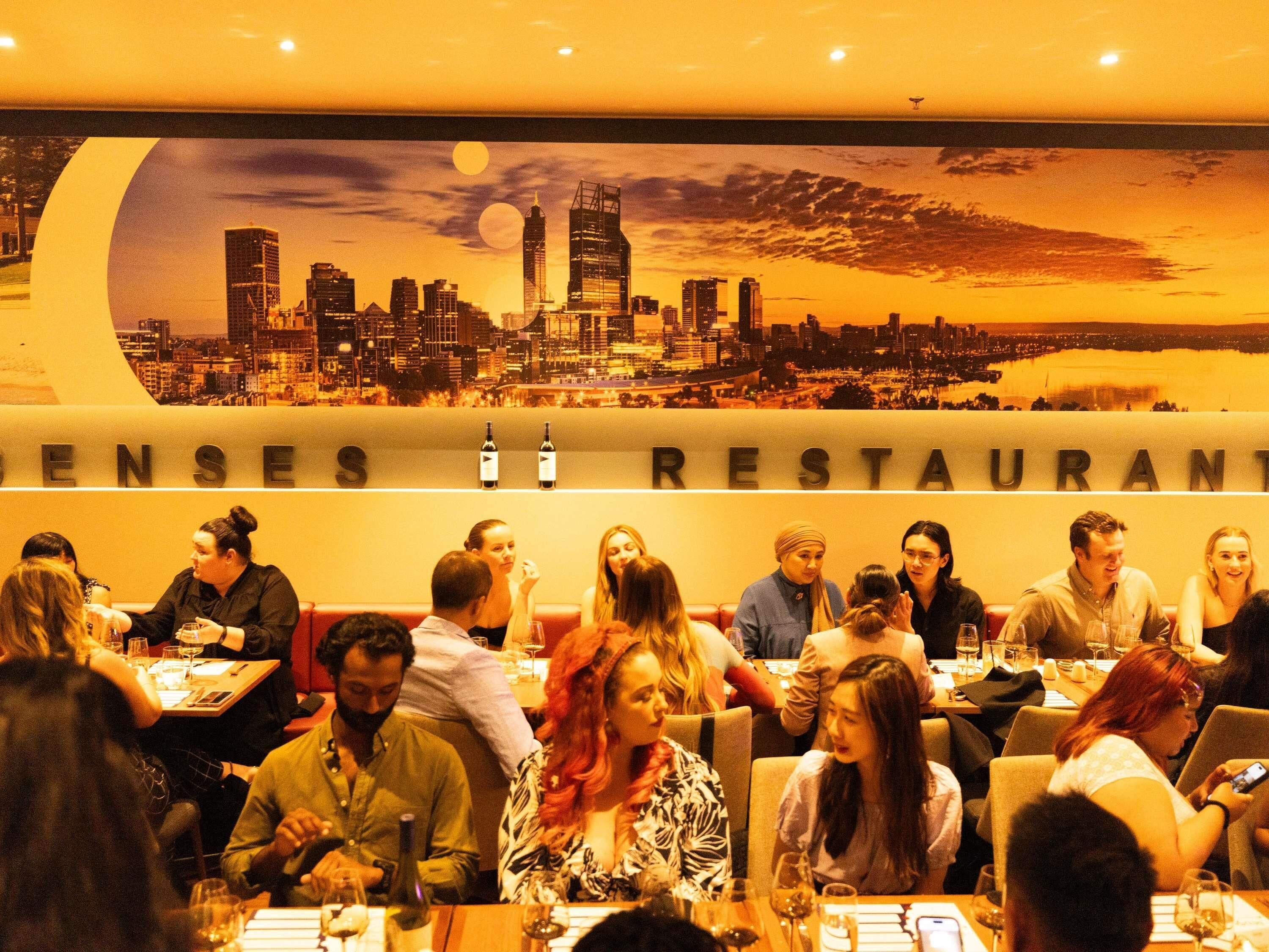 Ravintola, jonka seinällä on kaupunkimaisemaa esittävä seinämaalaus, pöydissä istuu asiakkaita, ja ulkona on kyltti, jossa lukee: ”SENSE RESTAURANT”.
