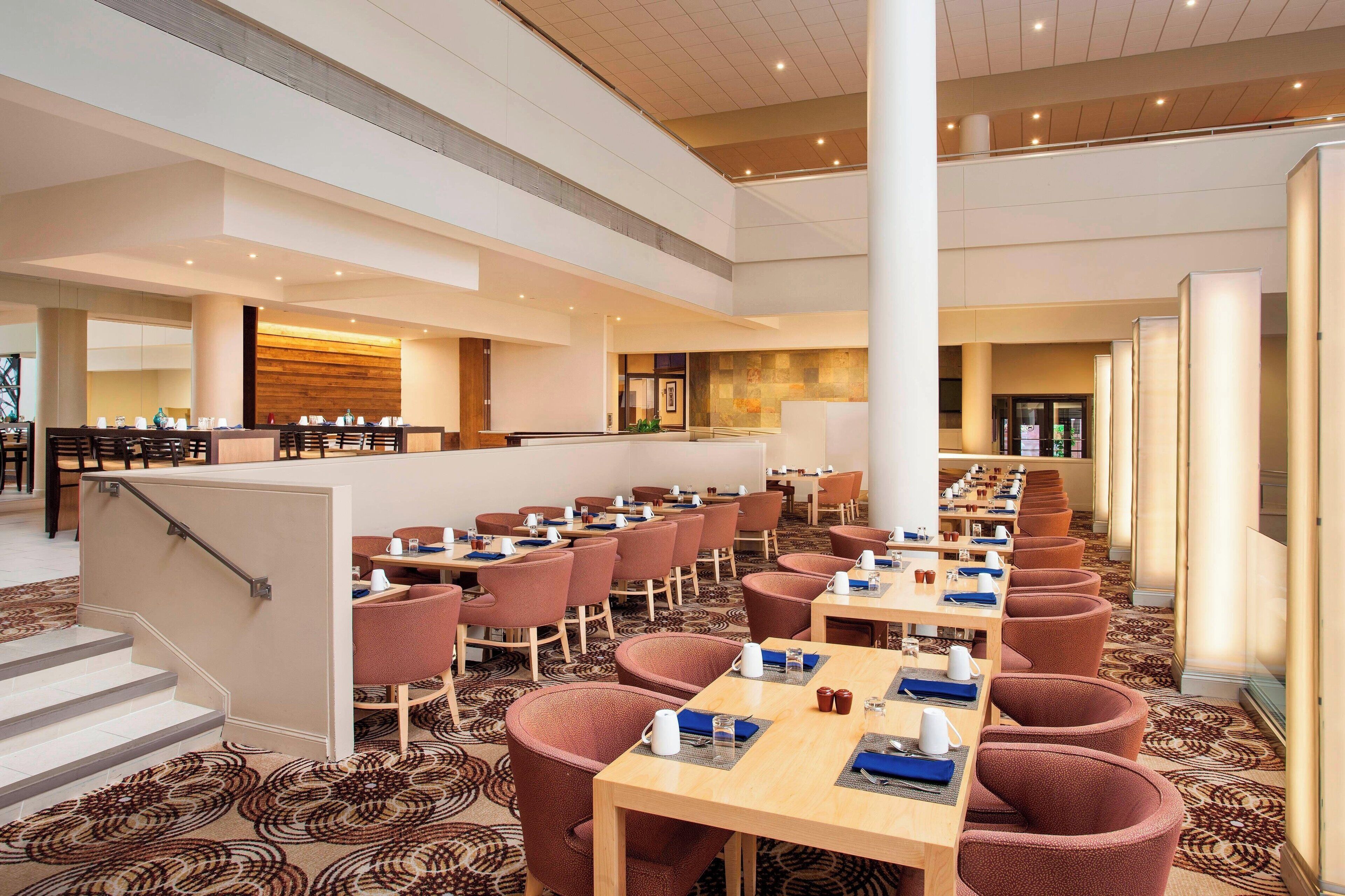 A spacious hotel lobby with multiple seating areas, a staircase, and a reception desk.